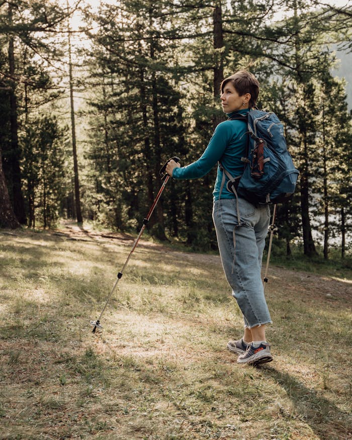 A woman enjoying a peaceful hike in a sunlit forest, using trekking poles and carrying a backpack.