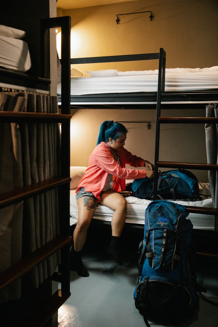 Young woman packs her backpack in a cozy hostel room, preparing for travel.